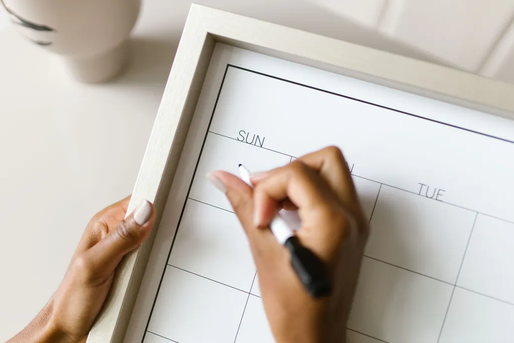 A hand writing on a whiteboard calendar with a marker