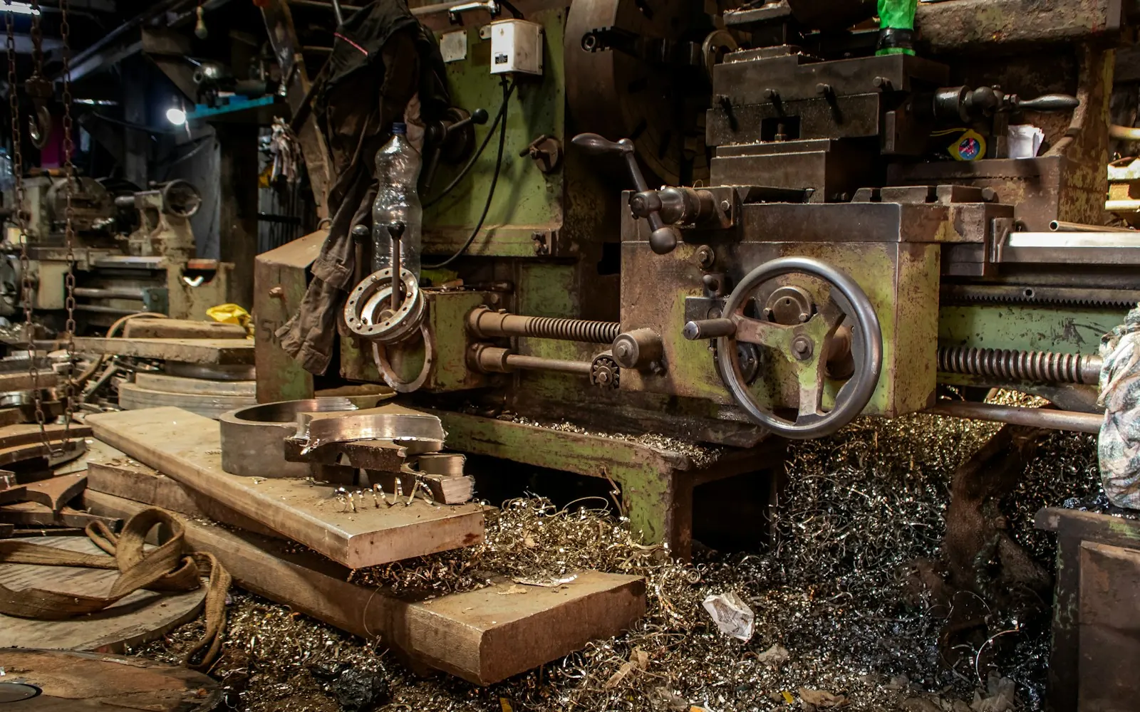 Older manual lathe on a shop floor surrounded by metal shavings and stock
